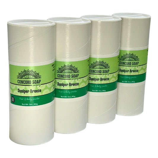 Four eco-friendly white cardboard shakers of handmade Juniper Breeze hair and body powder by Concord Soap Company, displayed on a solid white background. Each container has a green and white label featuring the company logo and product name. The tubes are arranged side by side in a row, showcasing the product packaging and branding. Natural talc-free powder in an airy juniper fragrance for a fresh scented skincare and personal hygiene product.