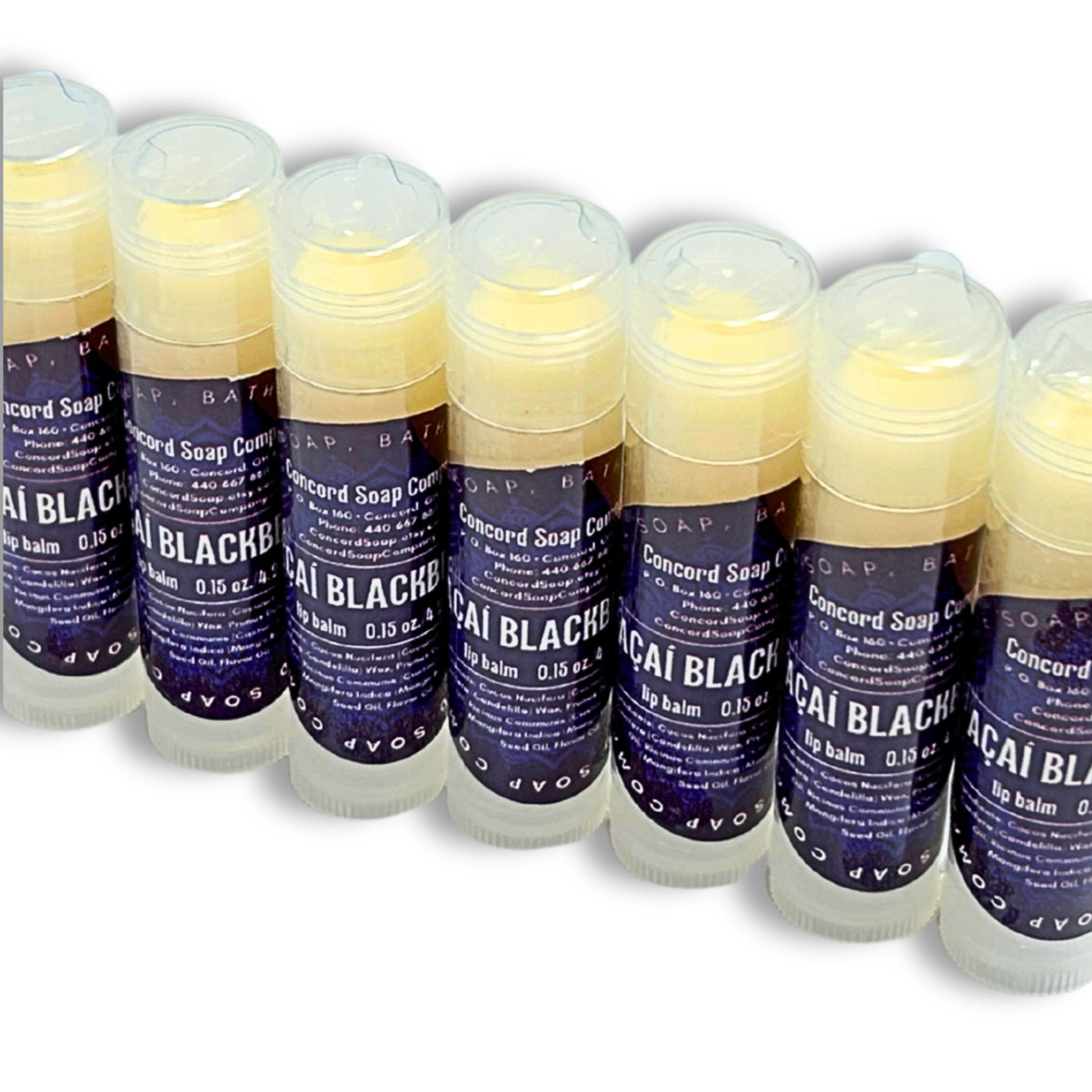 Slightly overhead view of Handmade Açaí Blackberry lip balm tubes arranged in a diagonal line. These natural lip balms by Concord Soap Company have a deep purple circle label with product and company details and is also shrink wrapped for safety. Listing is for ONE lip balm.