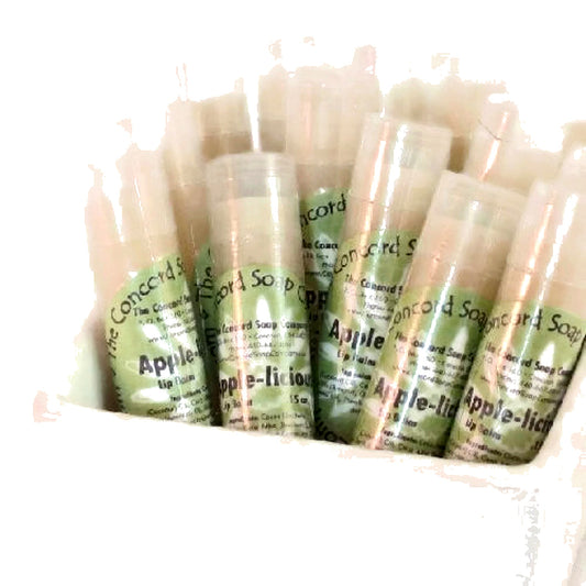 Multiple Apple-licious lip balm tubes with light green labels arranged in a white ceramic container, shown on a bright background.