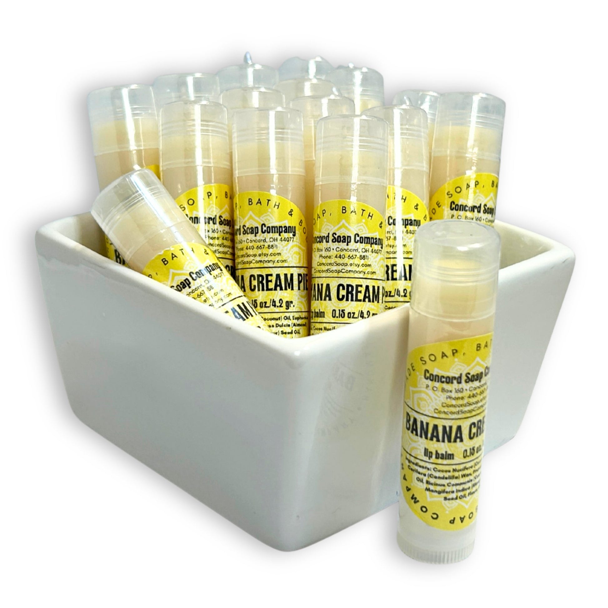 Handmade Banana Cream Pie lip balm tubes in bowl with one tube in front. This flavor of natural lip balms by Concord Soap Company is labeled with a bright yellow circular label, with product and company details, and is shrink wrapped for safety.