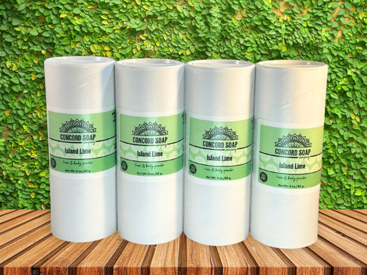 Four eco-friendly white cardboard shakers of handmade Island Lime hair and body powder by Concord Soap Company, displayed on a wood surface with a bright green leaf background. Natural talc-free powder in the coconut lime verbena fragrance for fresh, tropical scent skincare and personal hygiene.