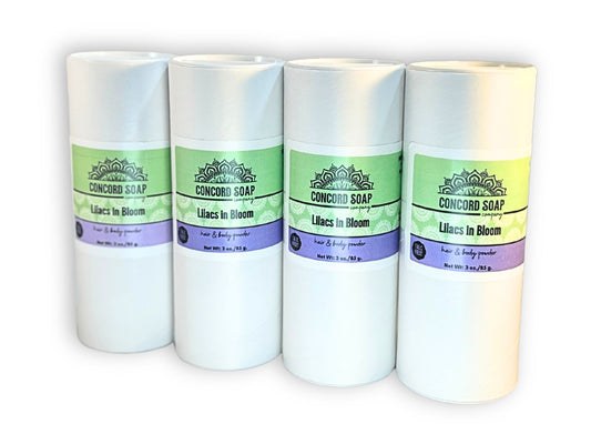 Four eco-friendly white cardboard shakers of handmade Lilacs in Bloom hair and body powder by Concord Soap Company, displayed on a solid white background. Natural talc-free powder in a true lilac fragrance for fresh, floral scent skincare and personal hygiene.