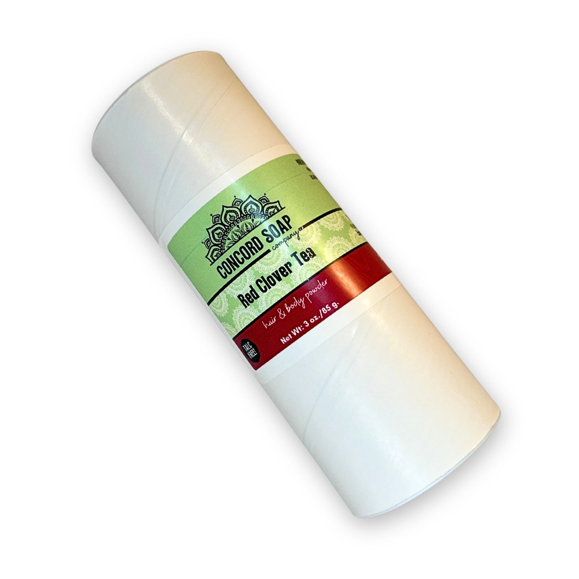 An eco-friendly white cardboard shaker of handmade Red Clover Tea hair and body powder by Concord Soap Company, displayed on a solid white background. The container has a green and white label featuring the company logo and product name. The tube is laying flat at a slight angle, showcasing the product packaging and branding. Natural talc-free powder in a best-selling sweet herby fragrance for a unique skincare and personal hygiene product.