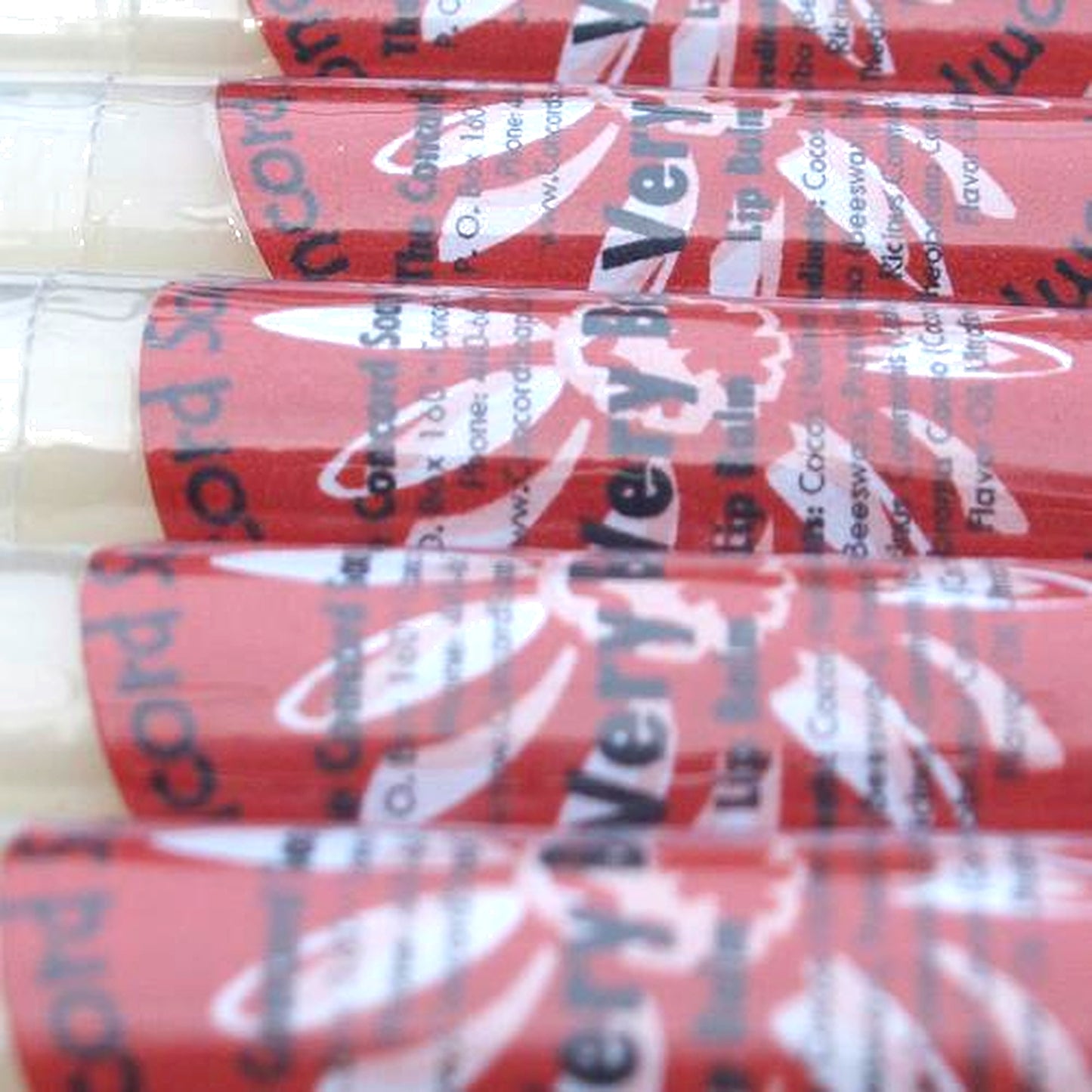 Close-up of Very Berry Sparkle lip balm tubes with red labels organized in a neat row.