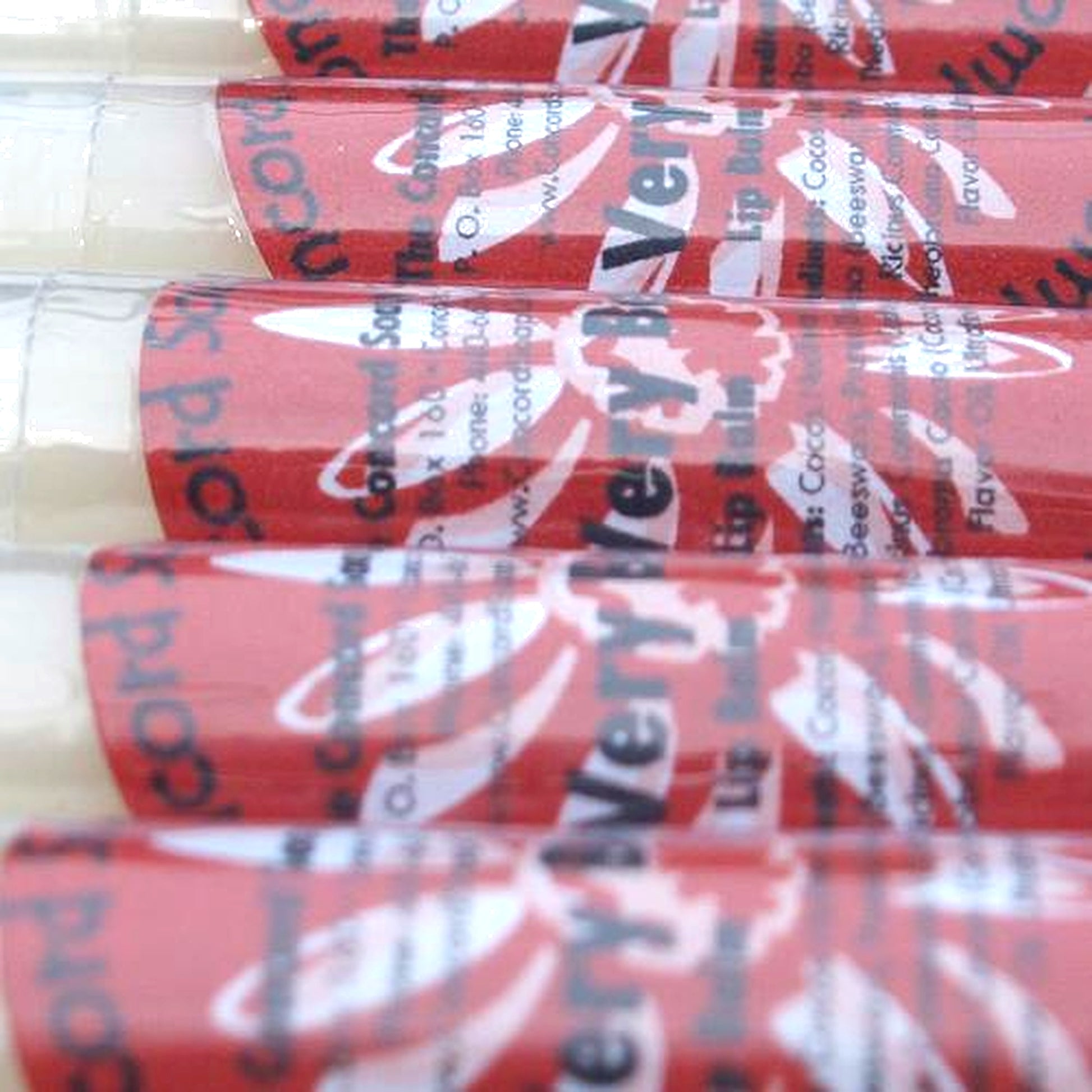 Close-up of Very Berry Sparkle lip balm tubes with red labels organized in a neat row.