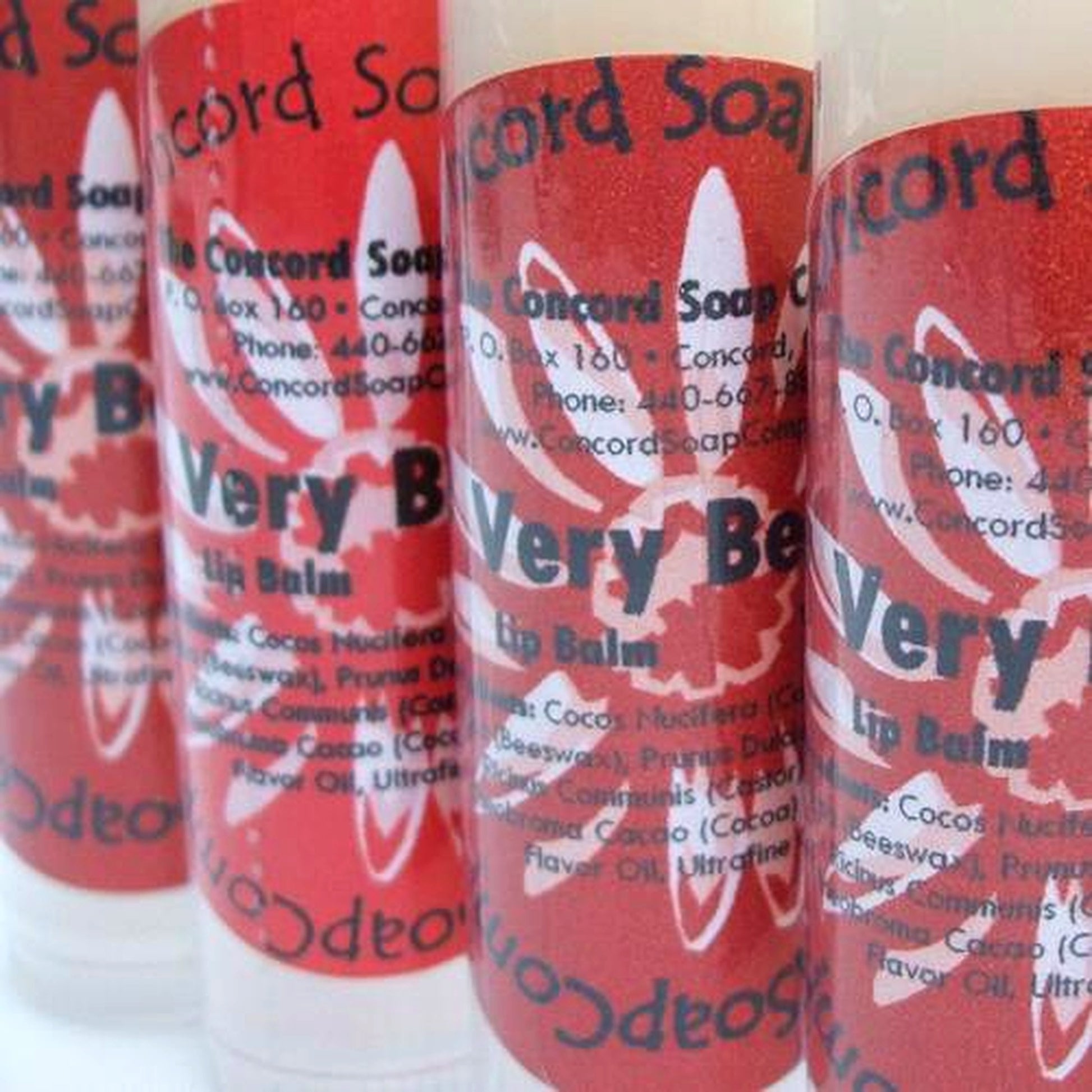 Close-up of Very Berry Sparkle lip balm tubes with red labels organized in neat rows on a white backdrop.