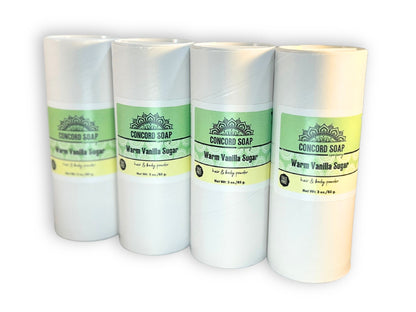 Four eco-friendly white cardboard shakers of handmade Warm Vanilla Sugar hair and body powder by Concord Soap Company, displayed on a solid white background. Each container has a green and white label. Natural talc-free powder in a sweet vanilla fragrance for a popular gourmand scent skincare and personal hygiene.