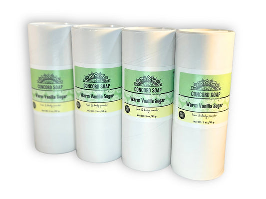 Four eco-friendly white cardboard shakers of handmade Warm Vanilla Sugar hair and body powder by Concord Soap Company, displayed on a solid white background. Each container has a green and white label. Natural talc-free powder in a sweet vanilla fragrance for a popular gourmand scent skincare and personal hygiene.