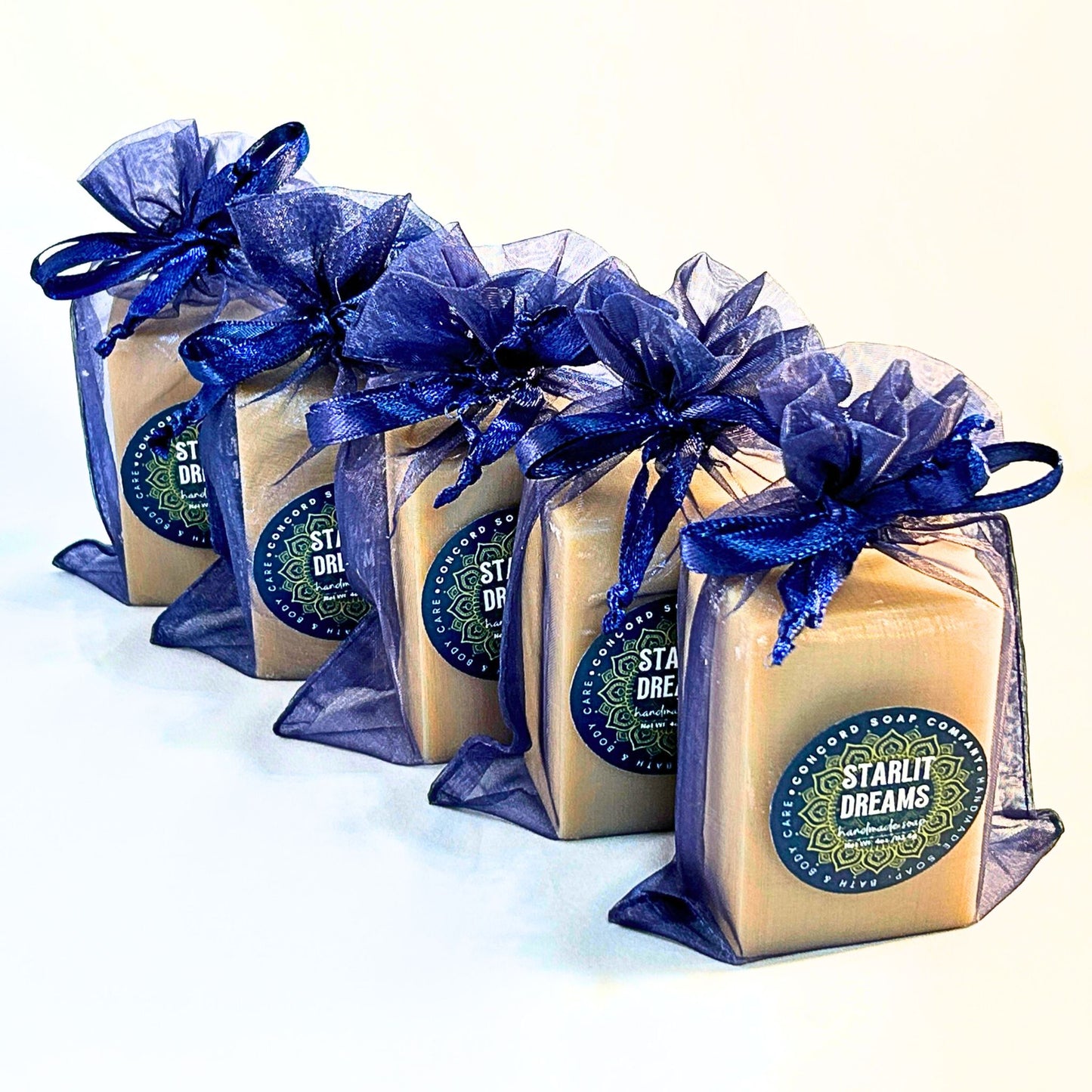 Row of Starlit Dreams handmade cold process soap bars wrapped in navy organza bags on a white background.