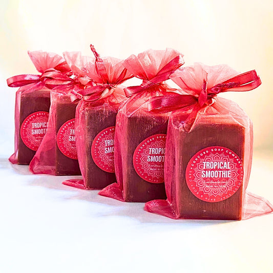 Five Tropical Smoothie handmade soap bars in bright pink organza gift bags with round Concord Soap Company labels, lined in a row. 