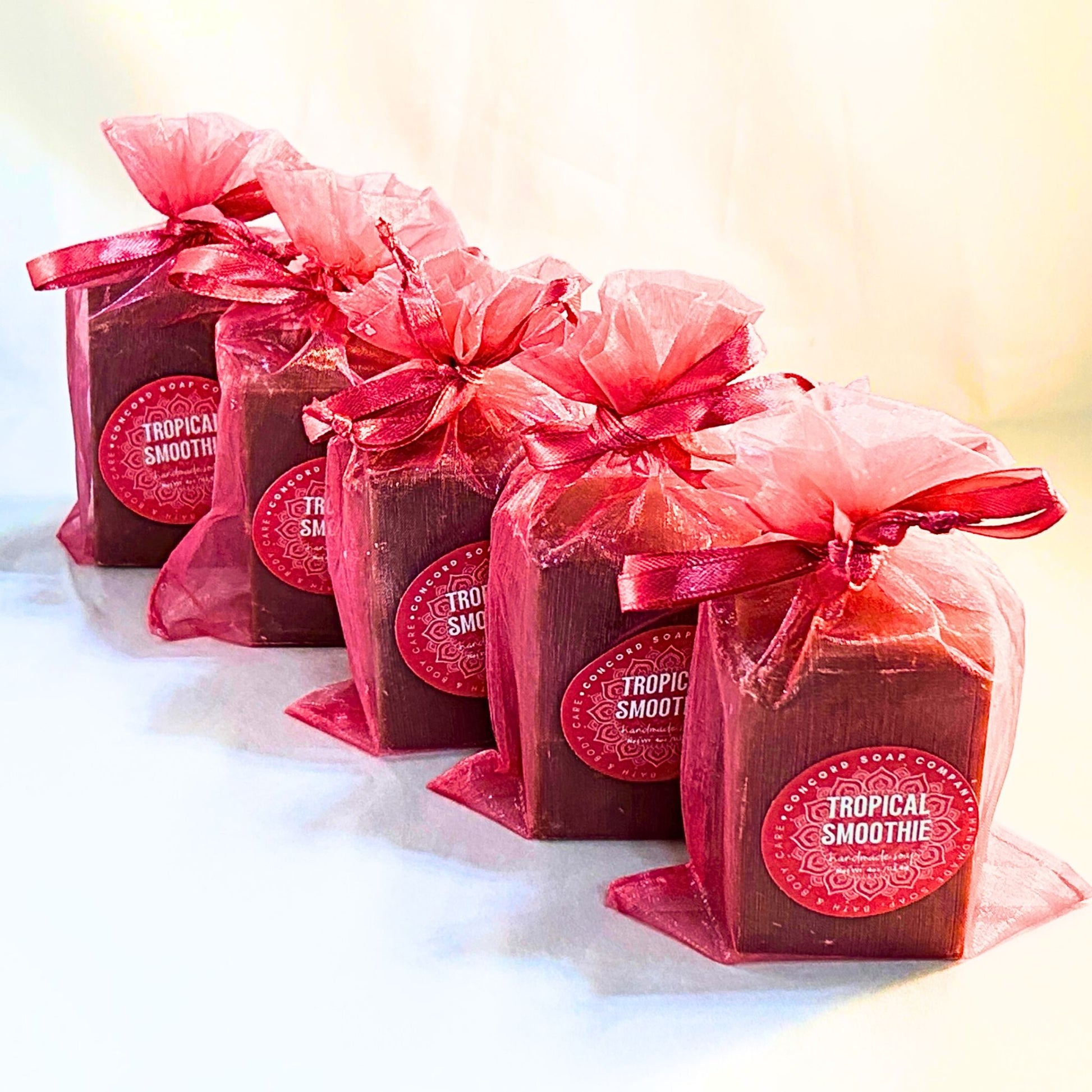 Diagonal lineup of five Tropical Smoothie vegan soap bars, wrapped in bright pink organza with Concord Soap Company labels. 