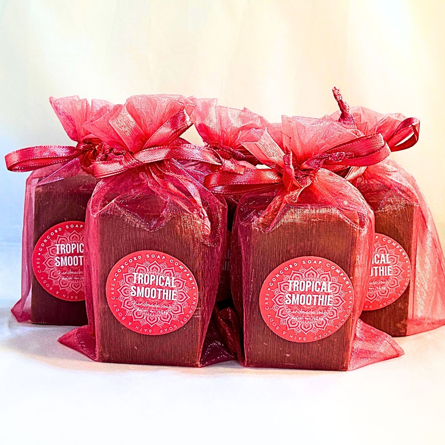 Front-facing group of five Tropical Smoothie handmade soaps in bright pink organza bags, labels visible against a light background. 