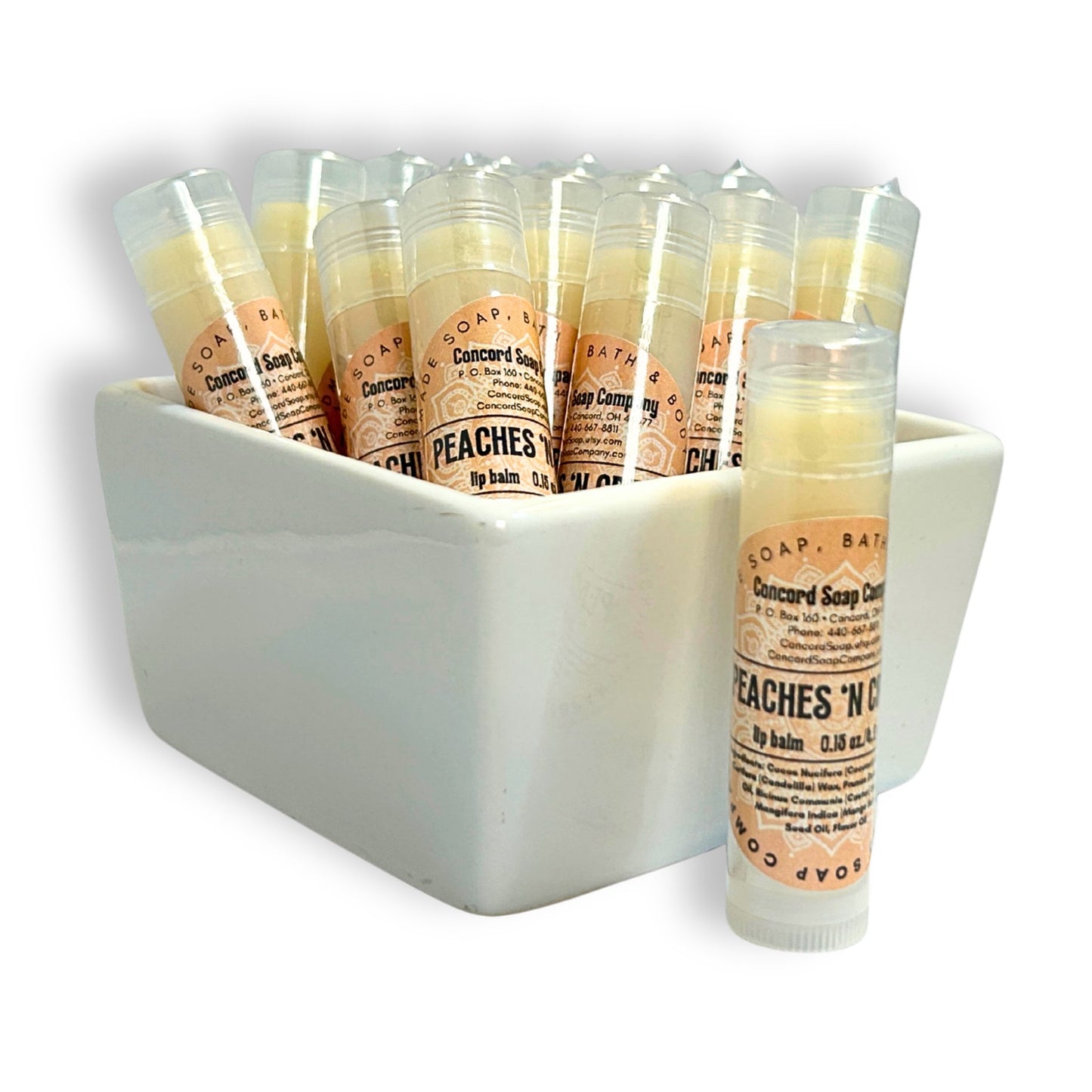 Handmade Peaches & Cream lip balm tubes in bowl with one tube in front. This flavor of natural lip balms by Concord Soap Company is labeled with a peach circular label, with product and company details, and is shrink wrapped for safety.