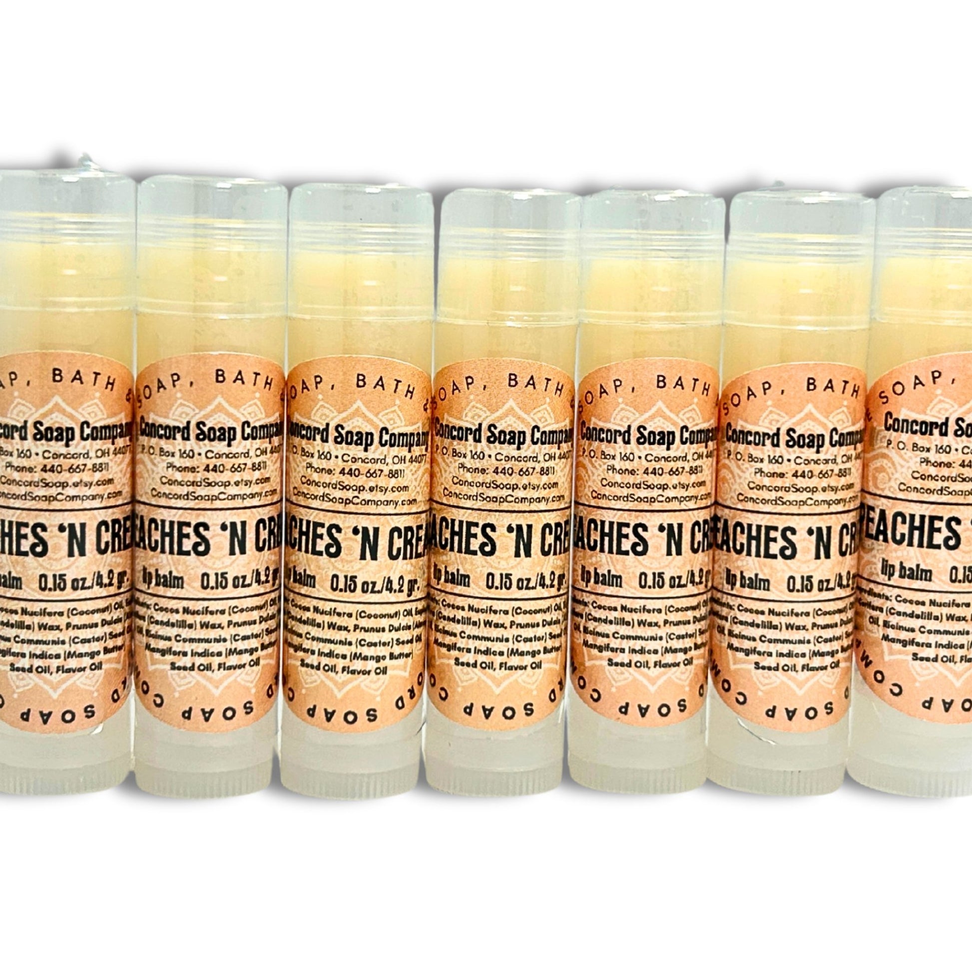 A line of Handmade Peaches & Cream lip balm tubes. Each of these natural lip balms by Concord Soap Company has a peach-colored circle label with product and company details and is shrink wrapped for safety.