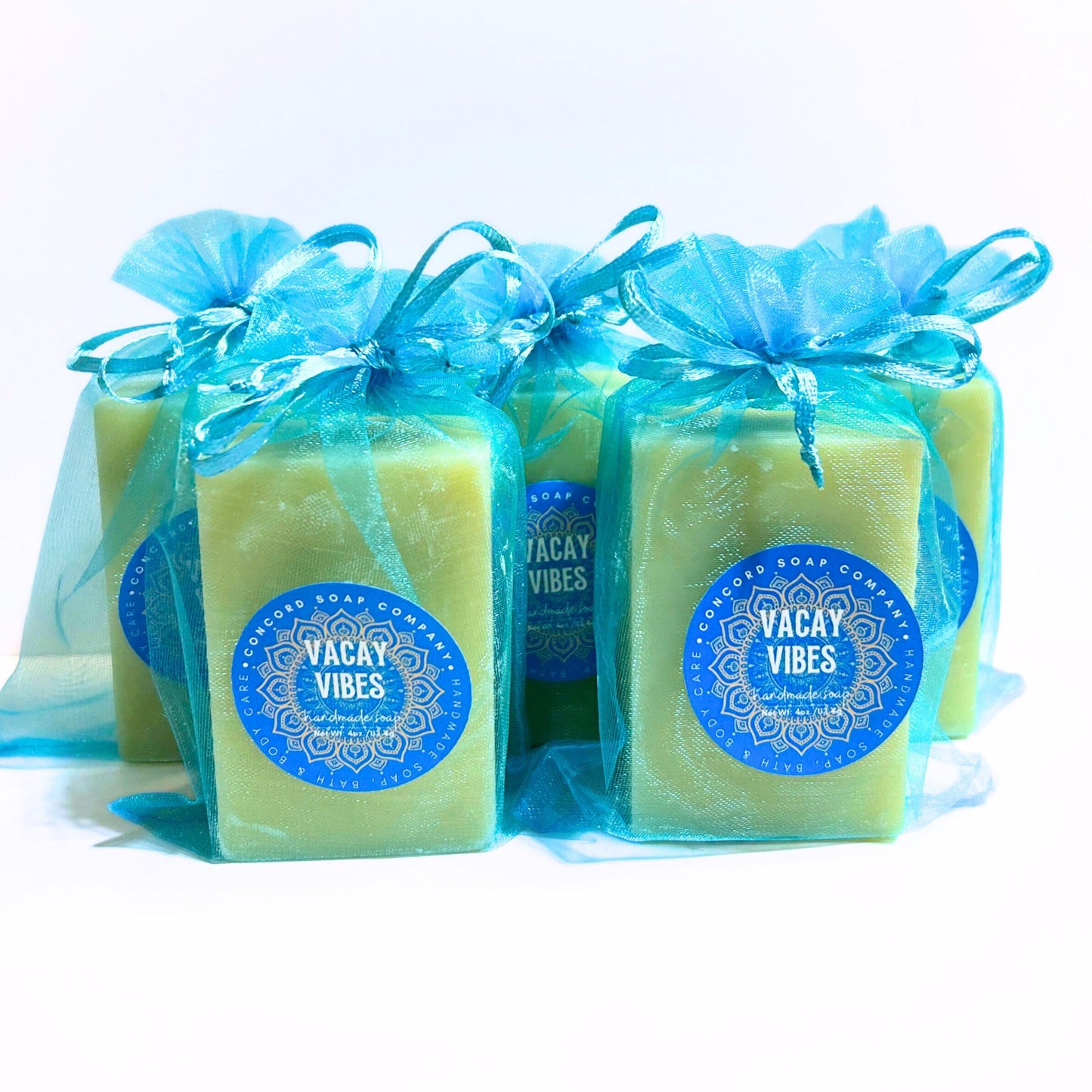 Group of Vacay Vibes handmade cold process soap bars standing upright in aqua organza gift bags with blue circular labels, summer beach scent.