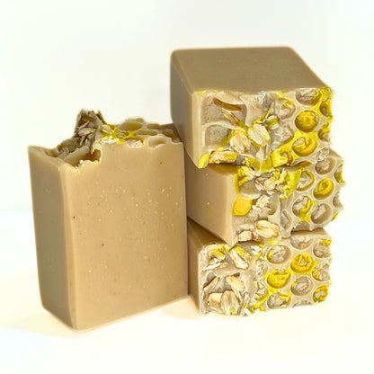Oat, Goat & Honey soap bars stacked together, showing tan bars with a honeycomb type texture on top accented with yellow gold mica and oats.