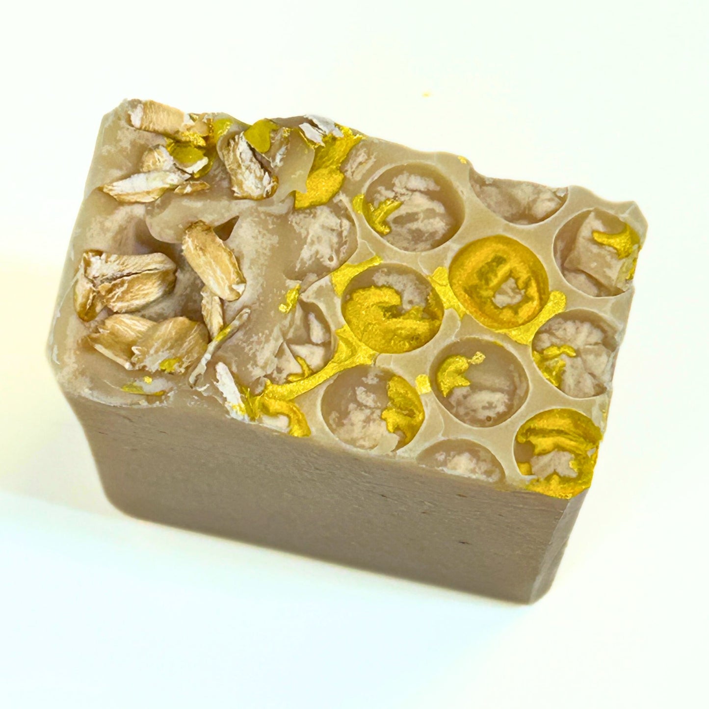 Top-down view of the soap bar showing the full honeycomb pattern with gold mica and clusters of oats.