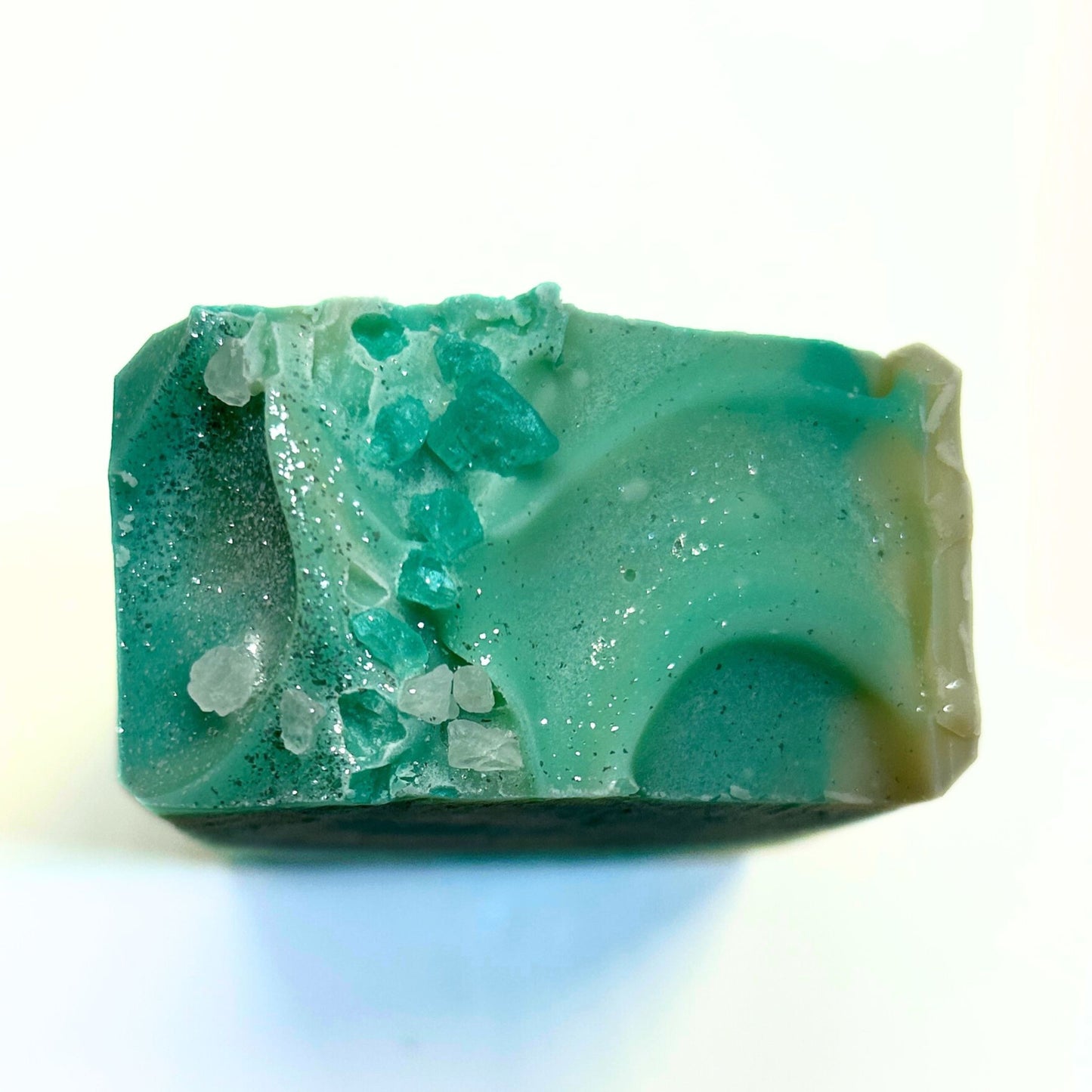 Top view of the soap bar featuring teal mica swirls, shimmery glitter and decorative rock salt crystals in natural and teal.