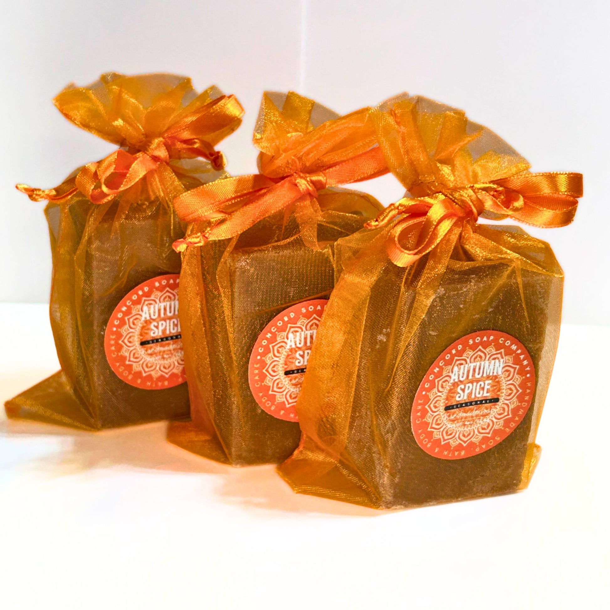 Three Autumn Spice soap bars wrapped in orange organza bags with orange ribbons.