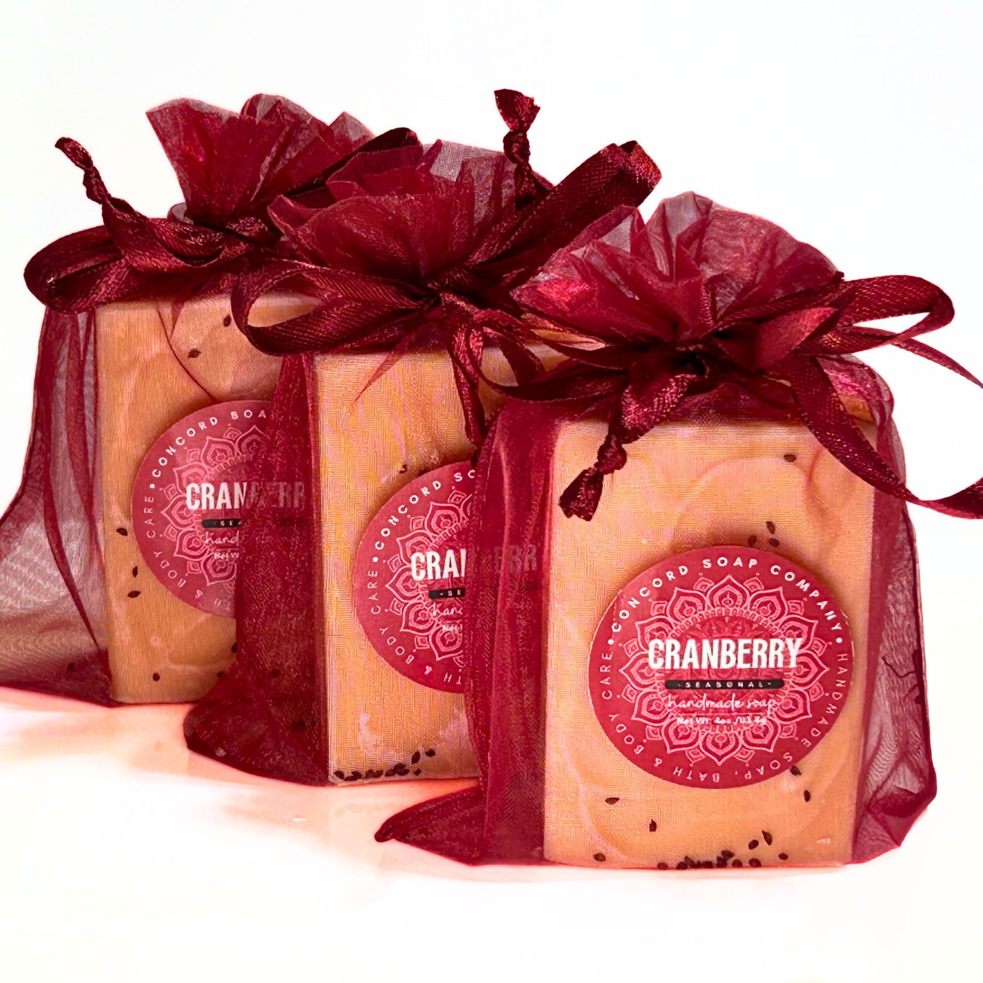 Three Cranberry soap bars wrapped in burgundy organza gift bags with matching bows.