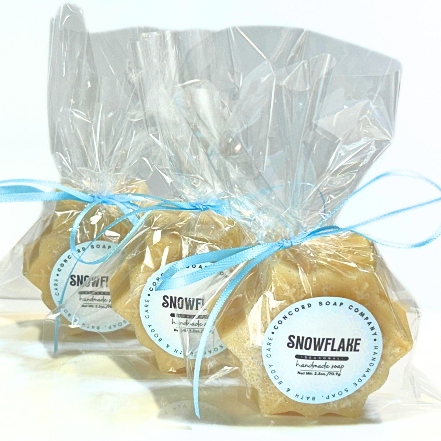 Clear cello-wrapped Snowflake soap bars tied with light blue ribbon, showing the snowflake shape through the packaging.