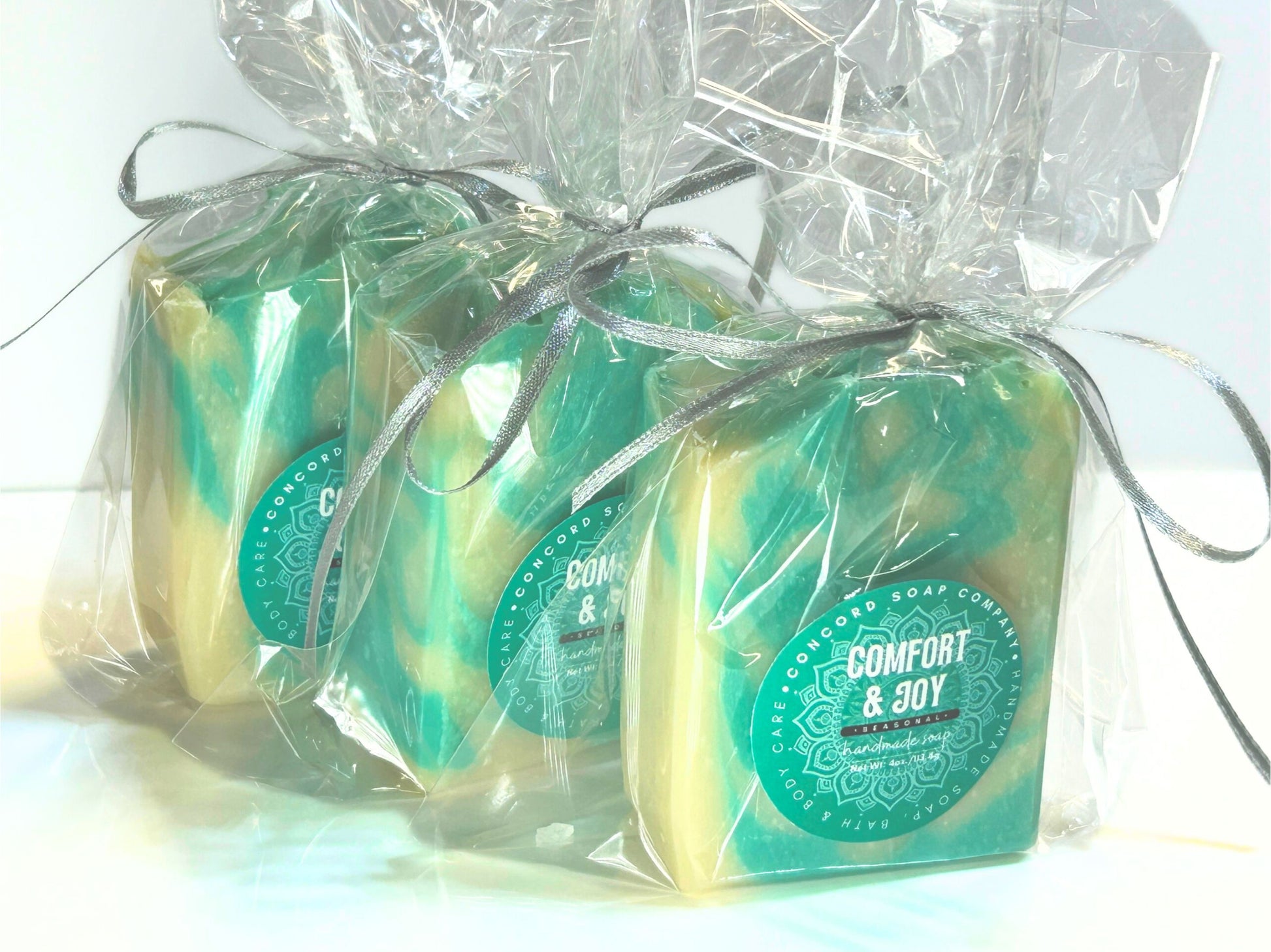 Side angle of a trio of Comfort & Joy wrapped soap bars tied with silver ribbon, arranged in a diagonal line.