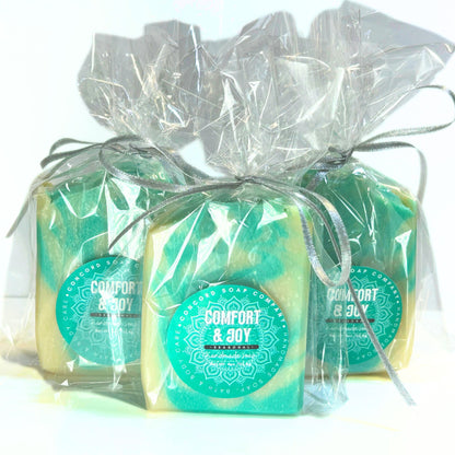 Three Comfort & Joy soap bars wrapped in clear cellophane with silver ribbons and teal round product labels.