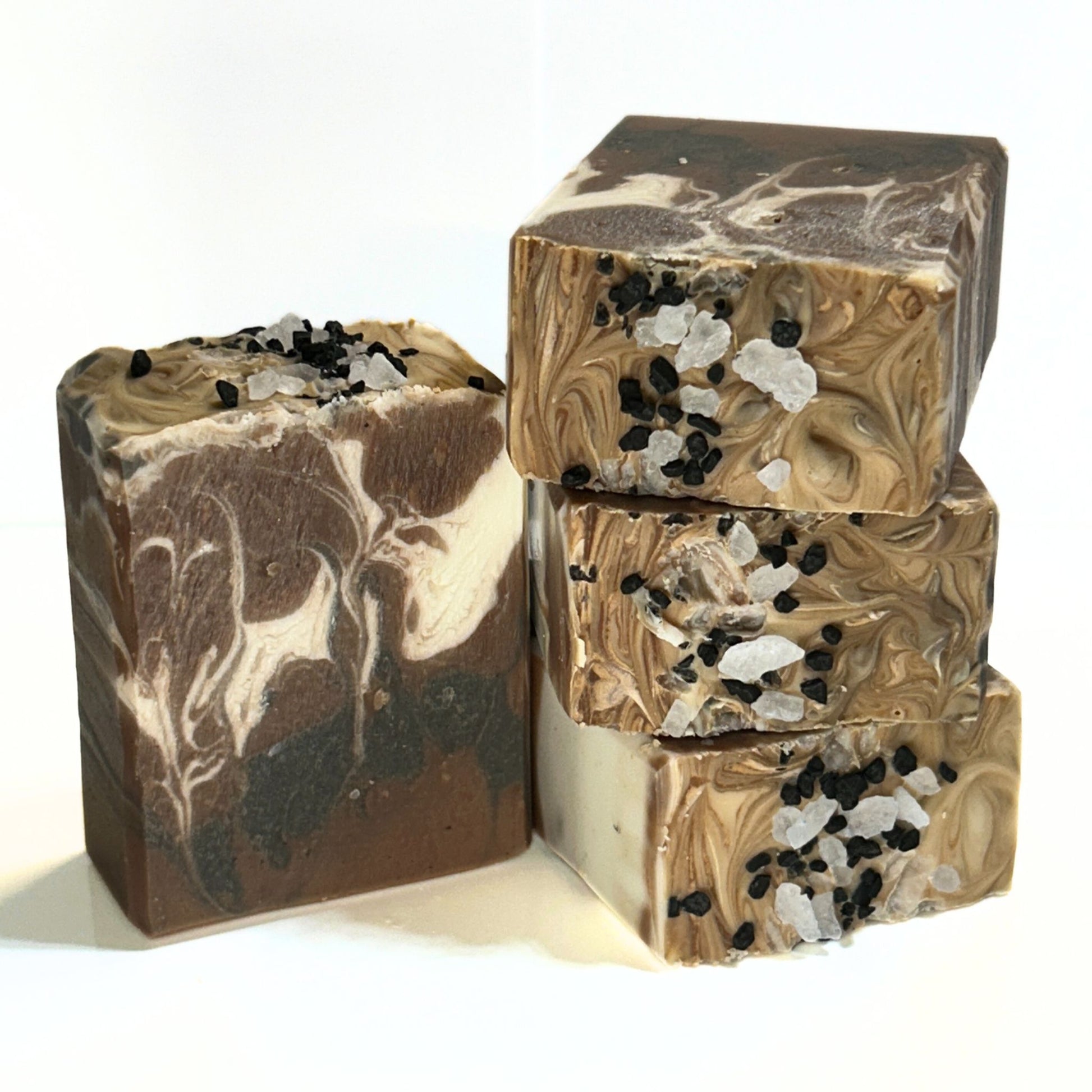 Handmade soap bars with brown, cream, and black swirls stacked together, topped with coarse natural rock salt and black Hawaiian salt.