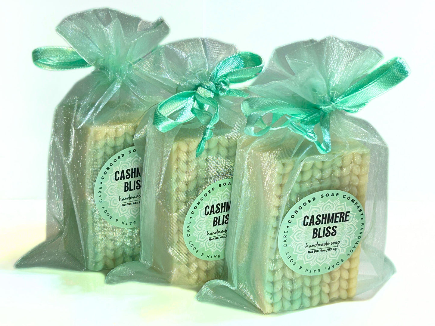 Front view of three Cashmere Bliss soaps in aqua organza gift bags lined up in a row.