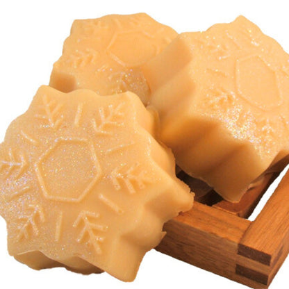 Three snowflake-shaped handmade soap bars with a pale golden color and subtle silver and blue shimmer, displayed on a small wooden soap dish.