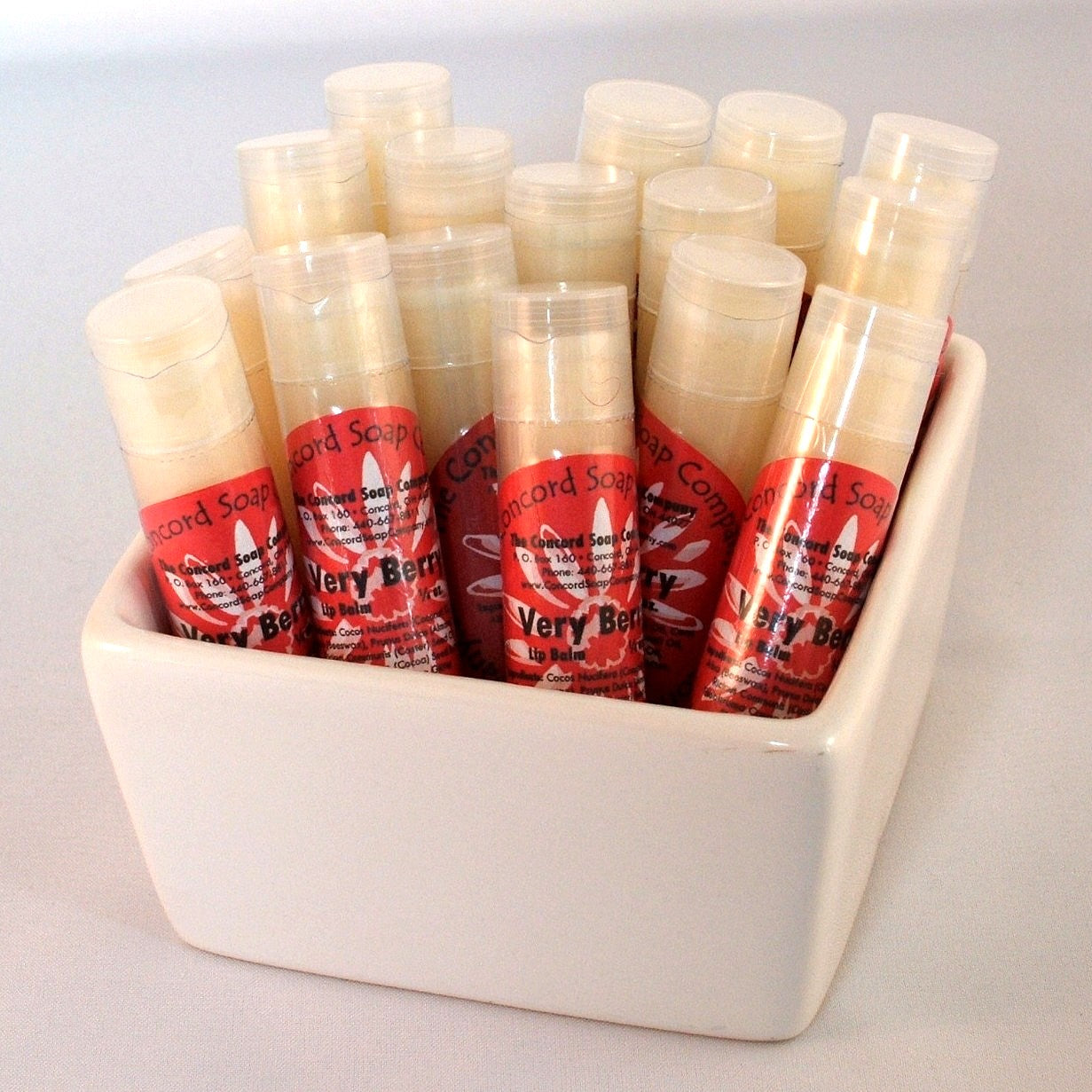 Very Berry Sparkle flavored lip balm tubes with red circular product labels displayed in a white ceramic dish.