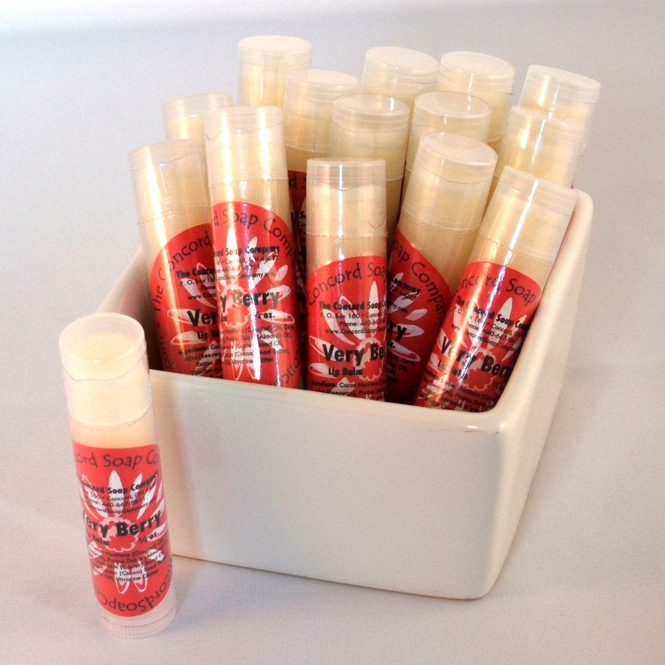Very Berry Sparkle flavored lip balm tubes with red circular product labels displayed in a white ceramic dish.
